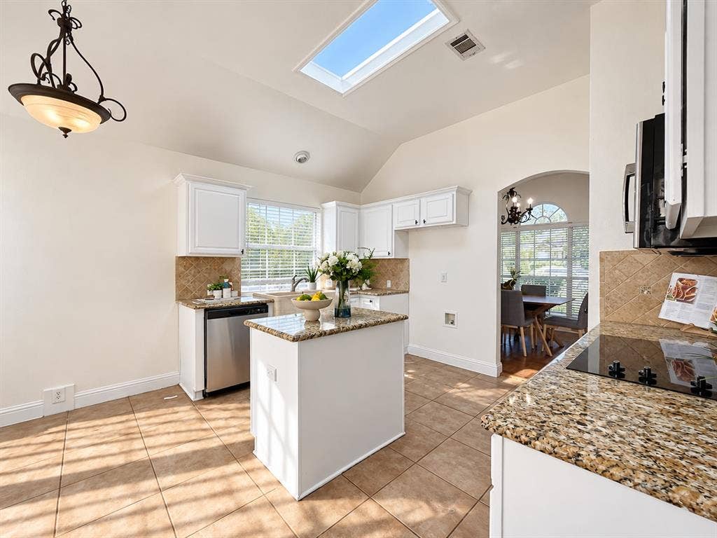 7514 Naples Lane, Frisco, TX 75035 Kitchen featuring white cabinetry, stone countertops, central island, skylight, and ceramic tile flooring