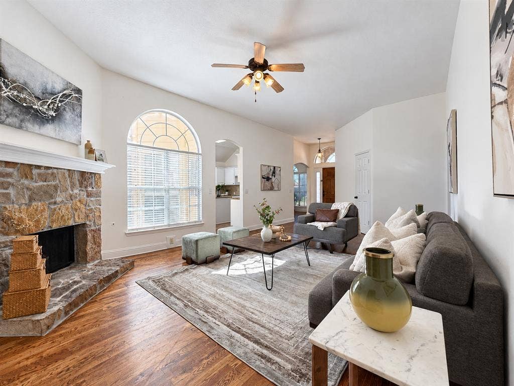 7514 Naples Lane, Frisco, TX 75035 Living area featuring a floor-to-ceiling natural stone fireplace, arched window with a grid design, wood-finish flooring, vaulted ceiling with a central fan, and an arched entry