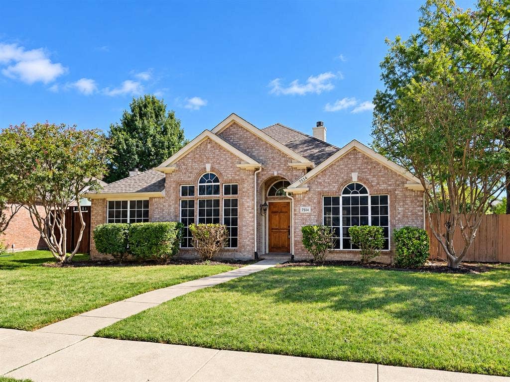 7514 Naples Lane, Frisco, TX 75035 Brick exterior featuring an arched entryway, grid-pattern windows, and a multi-gabled roofline, complemented by a front lawn and mature landscaping