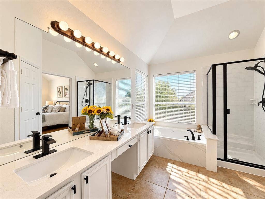 7514 Naples Lane, Frisco, TX 75035 Double vanity featuring white cabinetry, quartz countertops, undermount sinks with matte black fixtures, an oversized mirror, and a separate soaking tub and shower enclosure with matching matte black hardware