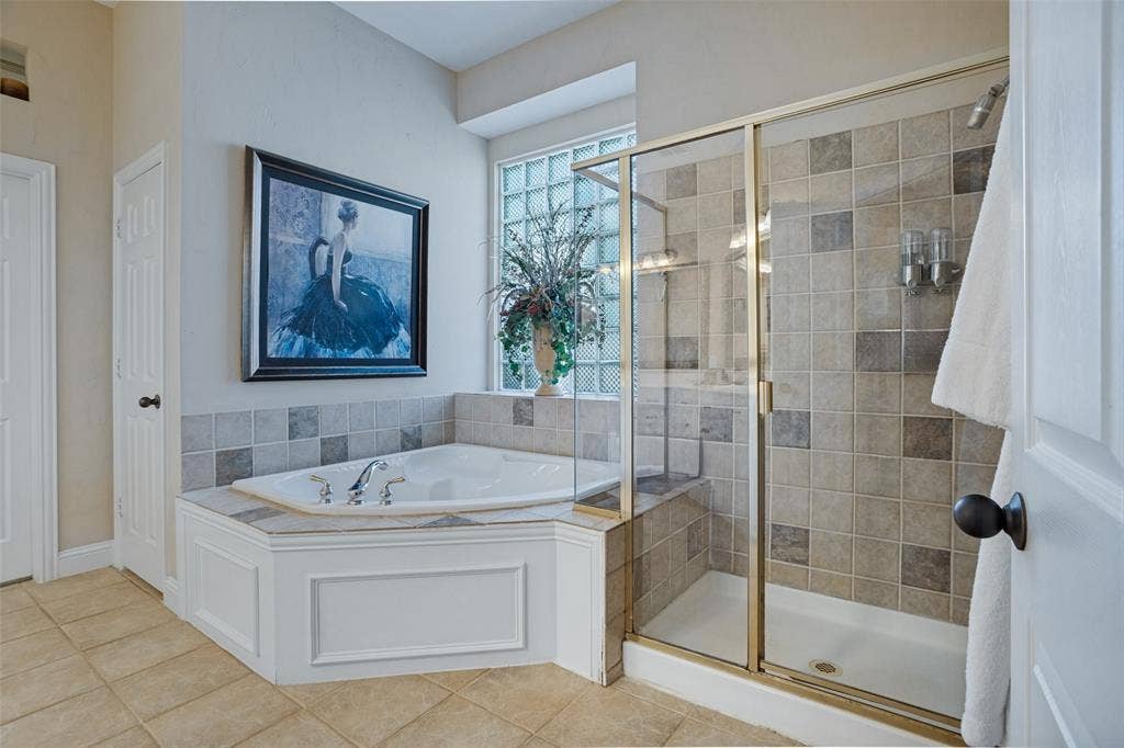 701 Crabapple Way, McKinney, TX 75072 Corner soaking tub with tile surround, glass block window, and walk-in shower featuring a brass-tone frame and multi-tonal square wall tile