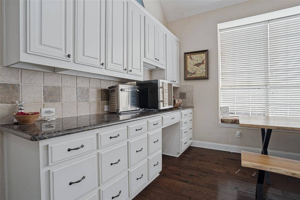 701 Crabapple Way, McKinney, TX 75072 White cabinetry with dark hardware, stone-finish countertops, square tile backsplash, built-in desk area, and wood-finish flooring