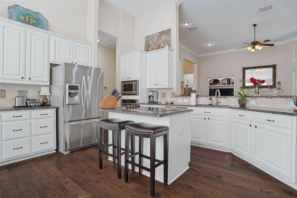 701 Crabapple Way, McKinney, TX 75072 Kitchen featuring white cabinetry, dark stone countertops, stainless steel appliances, a central island with counter seating, and wood-finish flooring