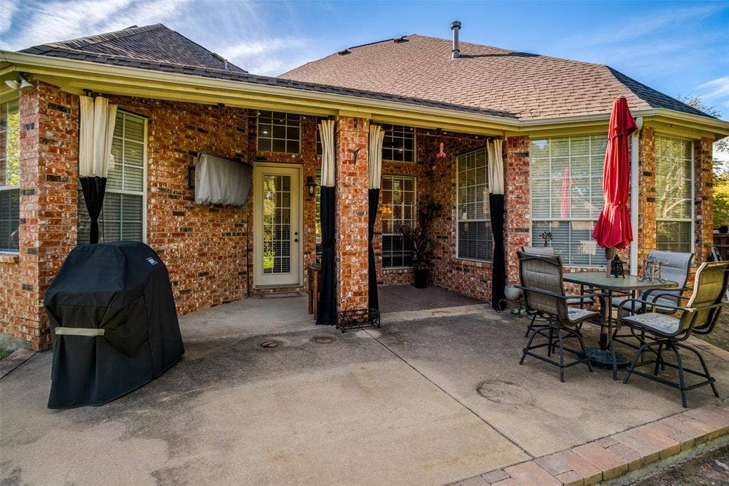 701 Crabapple Way, McKinney, TX 75072 Covered brick patio featuring a concrete floor, stone-trimmed border, and glass-paneled door