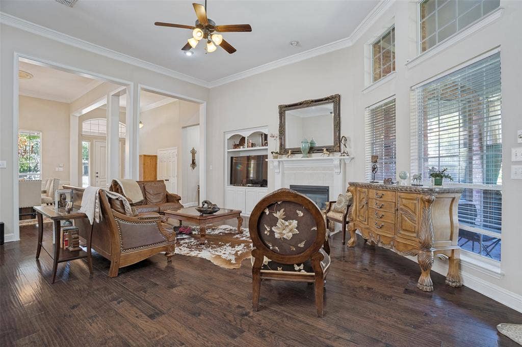 701 Crabapple Way, McKinney, TX 75072 High-ceiling living area featuring dark wood-finish flooring, a built-in fireplace with an ornate mantel, multi-pane transom windows, and crown molding