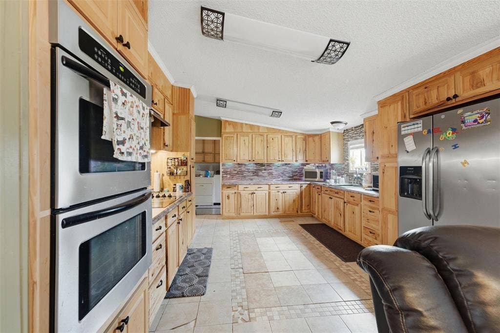 866 Old Church Rd, Waxahachie, TX 75165 Kitchen featuring wood cabinetry, stainless steel double wall oven, stainless steel refrigerator, tile flooring, and decorative stone-finish backsplash