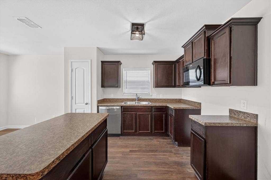 14276 Greenhaw Lane, Dallas, TX 75253 Kitchen featuring dark-finish cabinetry, an island with countertop seating, stone-patterned laminate countertops, stainless steel appliances, and wood-finish flooring
