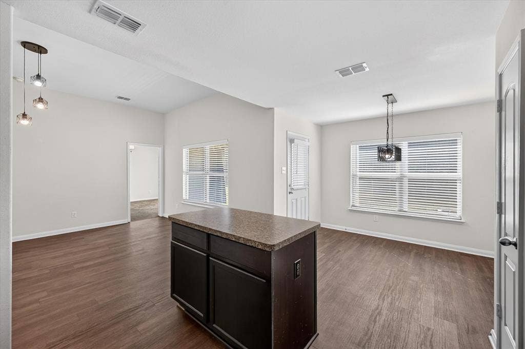 14276 Greenhaw Lane, Dallas, TX 75253 Wood-finish flooring, central kitchen island with a stone-composite countertop, dark-finish cabinetry, and decorative pendant lighting
