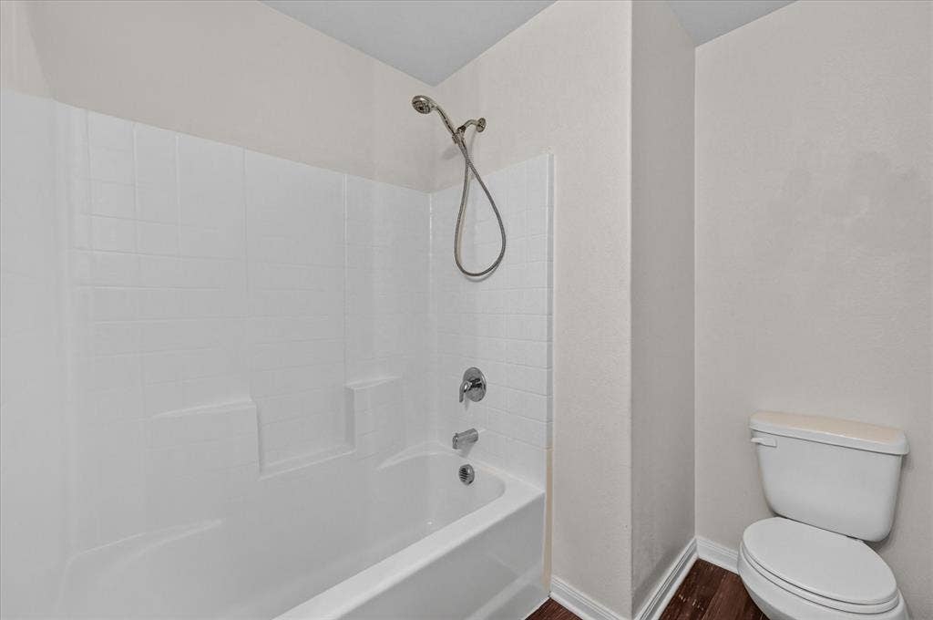 14276 Greenhaw Lane, Dallas, TX 75253 White acrylic tub and shower combination with a chrome handheld shower head, matching single-handle faucet, and wood-finish flooring