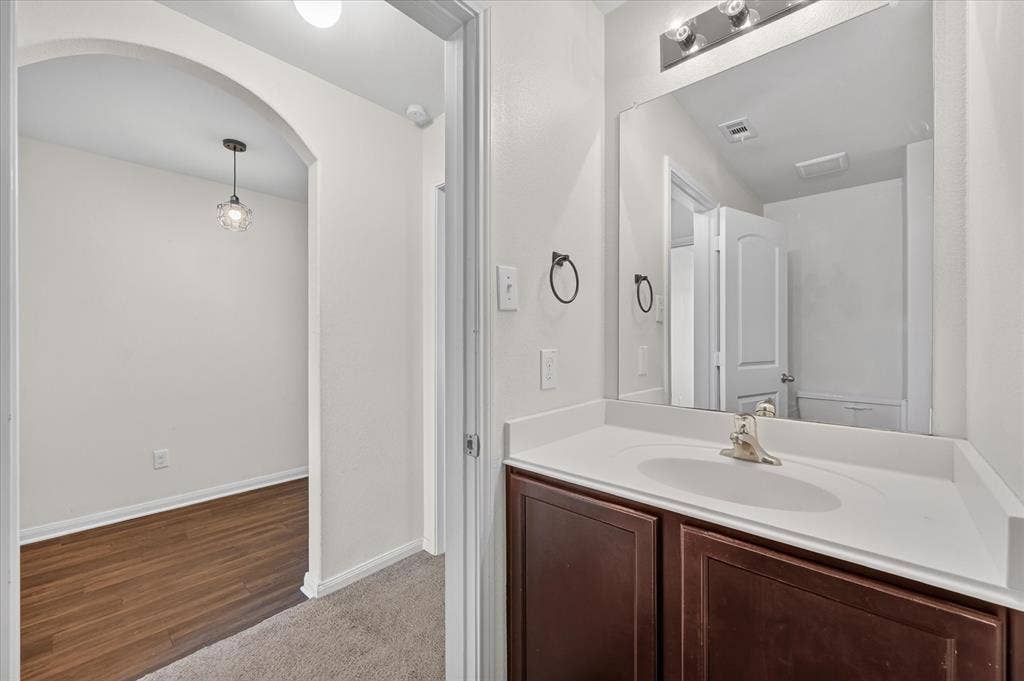 14276 Greenhaw Lane, Dallas, TX 75253 Vanity featuring a dark-finish wood cabinet, integrated sink, and wall-mounted light fixture, paired with a full-width mirror and an arched entryway