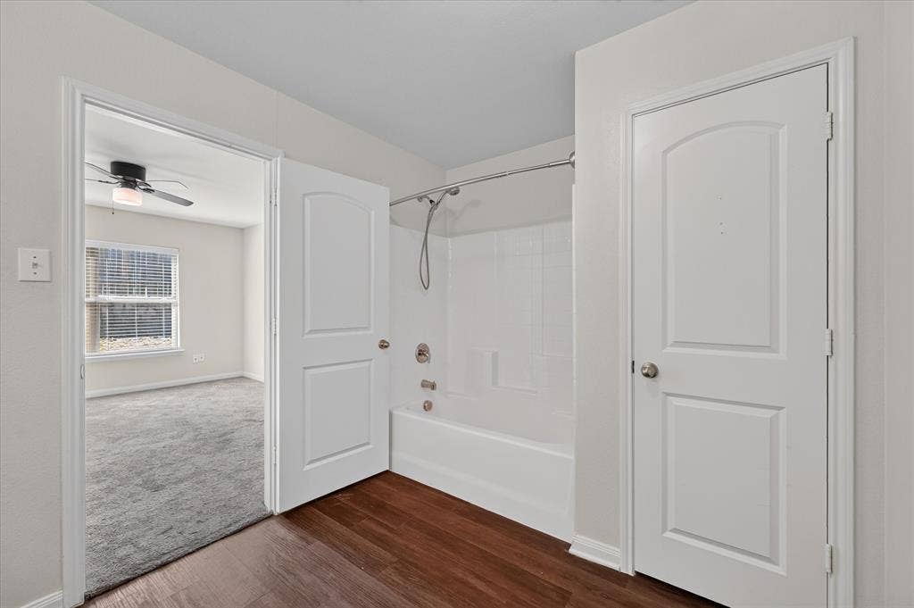 14276 Greenhaw Lane, Dallas, TX 75253 Bathroom featuring a tub-shower combination with a white surround, wood-finish flooring, two-panel interior doors, and a brushed nickel shower faucet