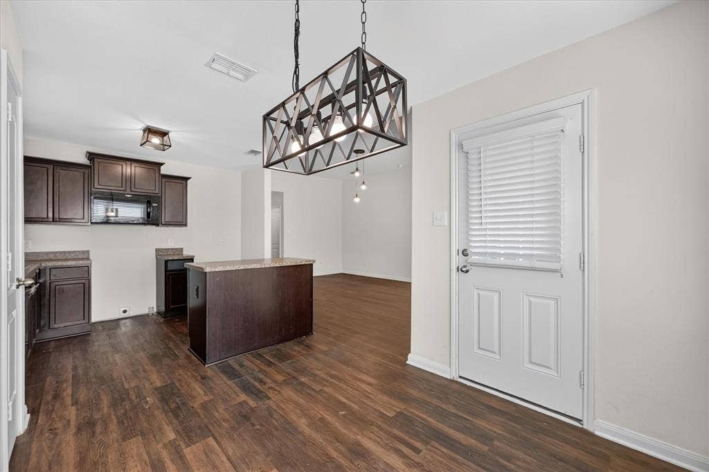 14276 Greenhaw Lane, Dallas, TX 75253 Dark-finish cabinetry, wood-finish flooring, central kitchen island, geometric metal-frame pendant lighting, and an exterior door with integrated blinds