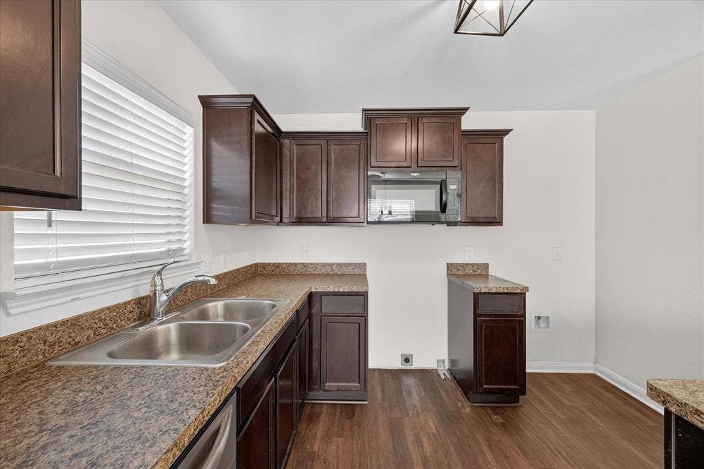 14276 Greenhaw Lane, Dallas, TX 75253 Dark-finish cabinetry paired with speckled laminate countertops, dual-basin stainless steel sink, built-in microwave, and wood-finish flooring