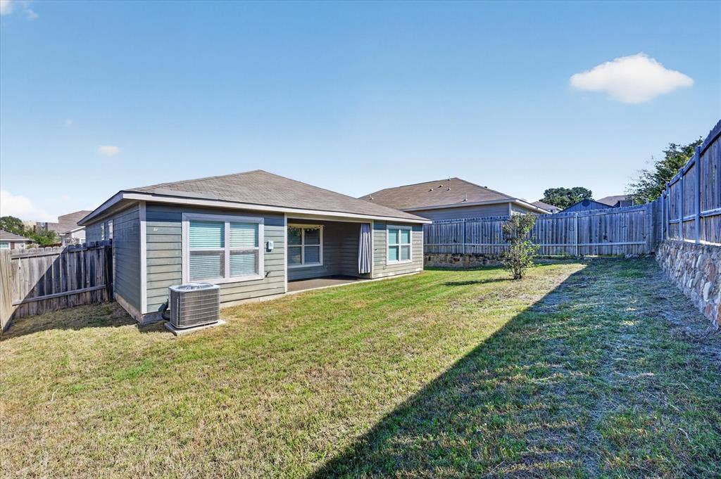 14276 Greenhaw Lane, Dallas, TX 75253 Rear exterior featuring horizontal lap siding, a covered patio, and a tiered retaining wall with stone-finish accents enclosed by wood fencing