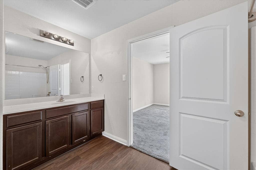 14276 Greenhaw Lane, Dallas, TX 75253 Bathroom featuring a dark wood-finish vanity, solid-surface countertop, full-width vanity mirror, and wood-finish flooring