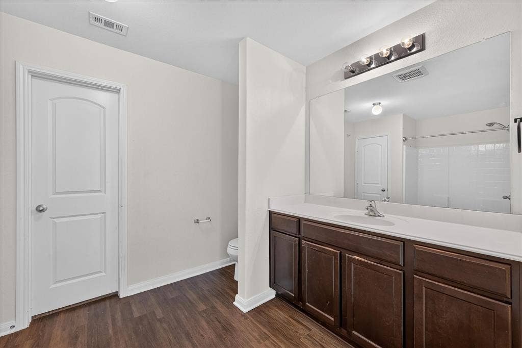 14276 Greenhaw Lane, Dallas, TX 75253 Bathroom featuring a dark wood-finish vanity, a full-width wall mirror, wood-finish flooring, and a single-basin countertop