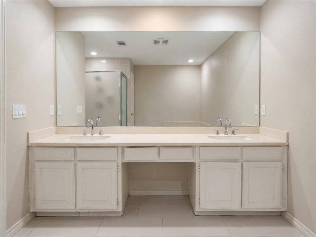 6011 Highplace Circle, Dallas, TX 75254 Double vanity featuring white cabinetry, a solid-surface countertop with dual integrated sinks, polished chrome faucets, and an expansive wall-to-wall mirror