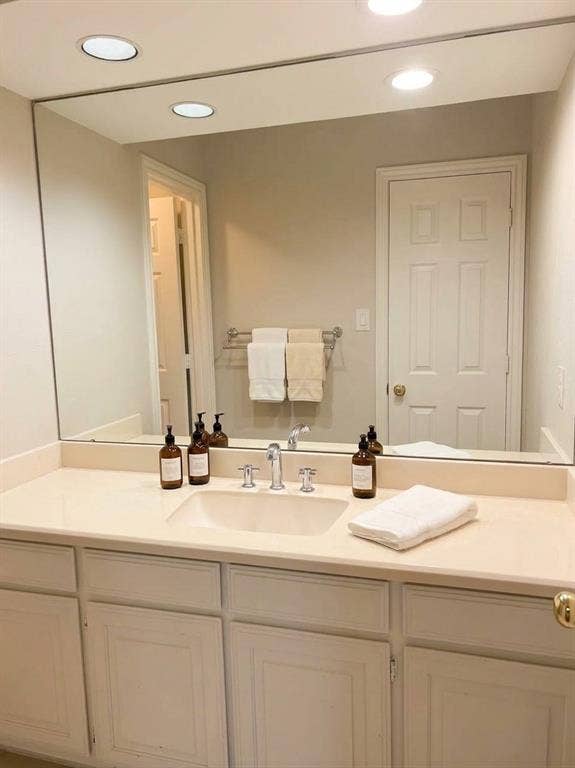 6011 Highplace Circle, Dallas, TX 75254 Vanity featuring a solid-surface countertop, integrated rectangular sink, chrome widespread faucet, and recessed-panel cabinetry with a large wall-mounted mirror