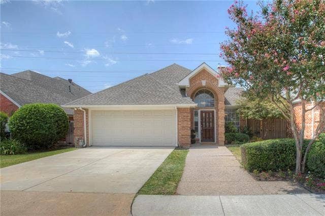 4005 Bramley Way, Plano, TX 75093 Brick exterior facade featuring a covered entryway with an arched stone surround, an attached two-car garage, and a concrete driveway