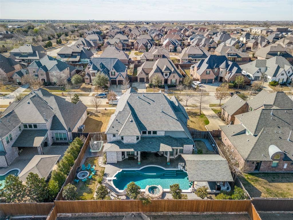 Aerial view of the back of property with the pool, the slide, the diving board, the spa, the tanning bed, the in-pool barstools, and the pergola with the outdoor kitchen.