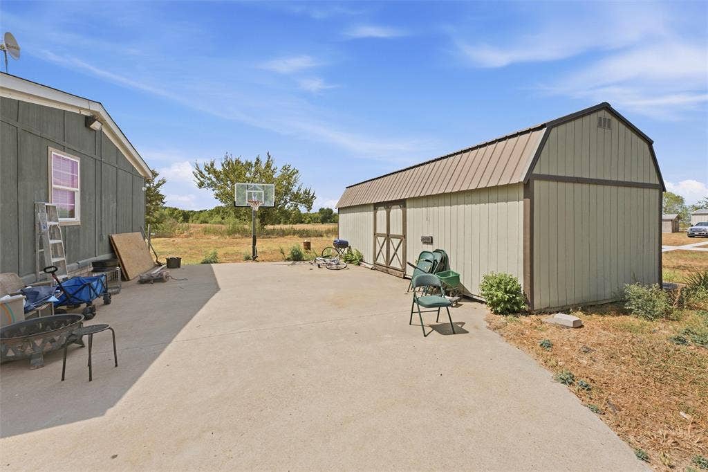 902 Old Church Rd, Waxahachie, TX 75165 Concrete patio featuring a detached storage shed with a metal roof and a permanent basketball goal