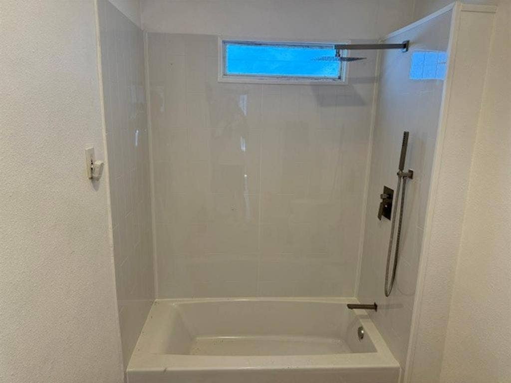 422 S Glasgow Drive, Dallas, TX 75223 Bathtub with white surround, rainfall showerhead, handheld shower, and horizontal window