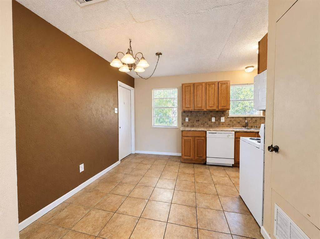 2418 Fulton Drive, Mesquite, TX 75150 Kitchen featuring wood cabinetry, stone-finish tile backsplash, tile flooring, and a multi-arm chandelier