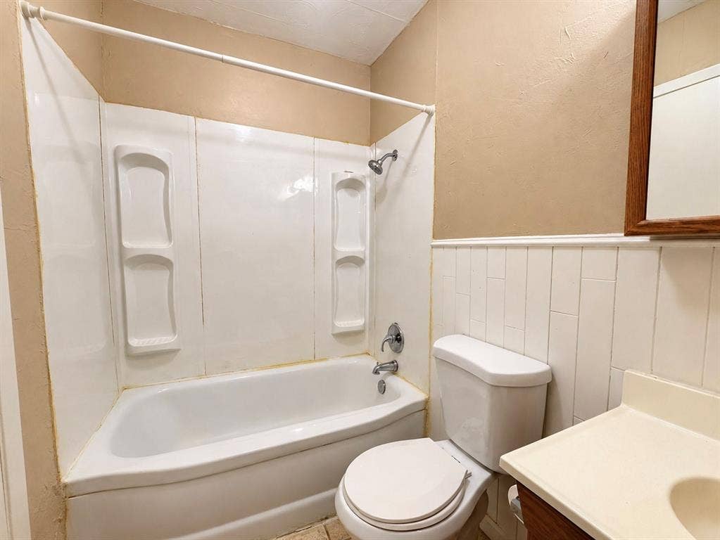 2418 Fulton Drive, Mesquite, TX 75150 Bathroom featuring a tub-shower combination with integrated shelving, vertical wainscoting, and a vanity with a molded sink