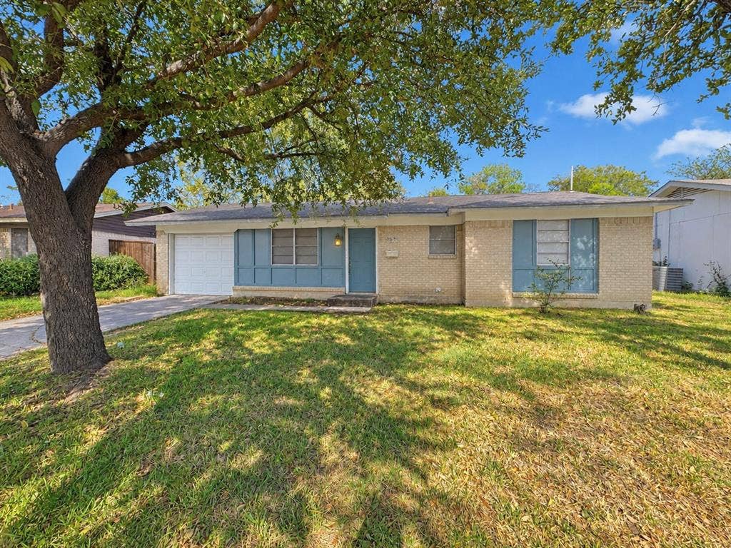 2418 Fulton Drive, Mesquite, TX 75150 Single-story exterior featuring a light-toned brick facade, panelized window shutters, an attached single-car garage, and mature tree canopy on a grass-covered lot