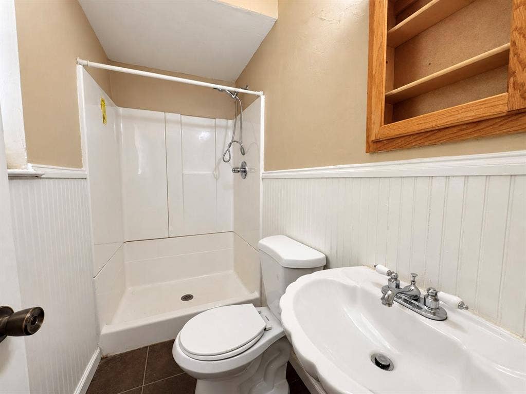 2418 Fulton Drive, Mesquite, TX 75150 Bathroom featuring a white molded shower surround, white beadboard wainscoting, a wall-mounted wood-finish medicine cabinet, and a scalloped porcelain sink with a polished chrome faucet