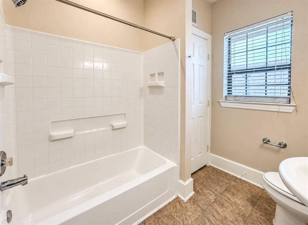 4227 Delano Place, Dallas, TX 75204 Bathroom featuring a white tile tub surround with integrated shelving, metallic fixtures, a window with horizontal blinds, and tile flooring