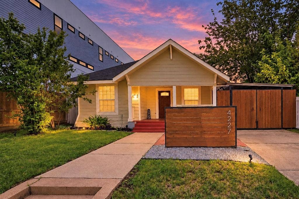 4227 Delano Place, Dallas, TX 75204 Exterior facade featuring horizontal siding, a covered front porch, a custom wood-slat privacy screen, a concrete driveway, and an attached storage structure