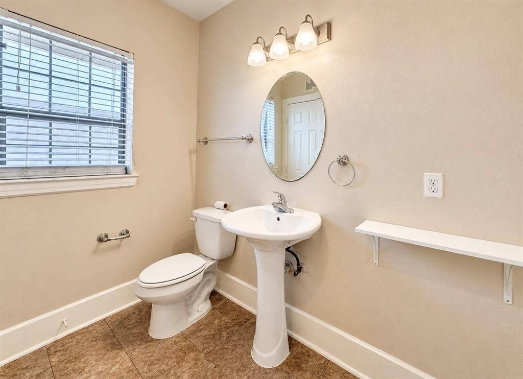 4227 Delano Place, Dallas, TX 75204 Bathroom featuring tile flooring, a porcelain pedestal sink with a chrome faucet, an oval wall-mounted mirror, three-light vanity fixture, and a built-in wall shelf