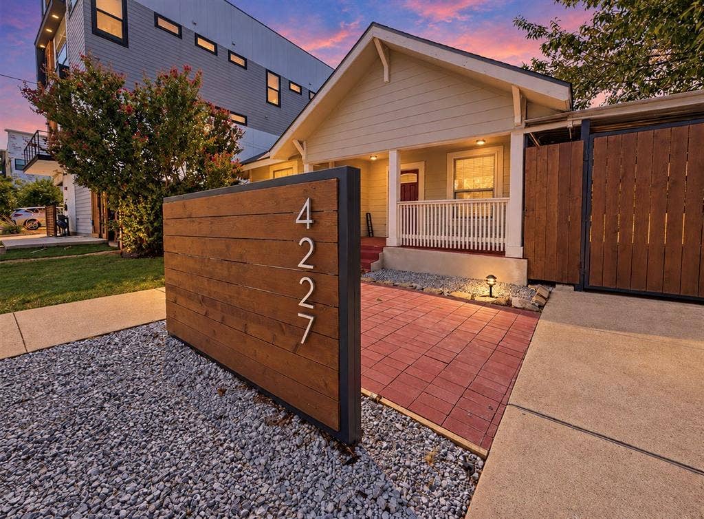 4227 Delano Place, Dallas, TX 75204 Exterior facade featuring horizontal wood-plank accent wall, paved brick patio, covered front porch with railing, and gravel landscaping