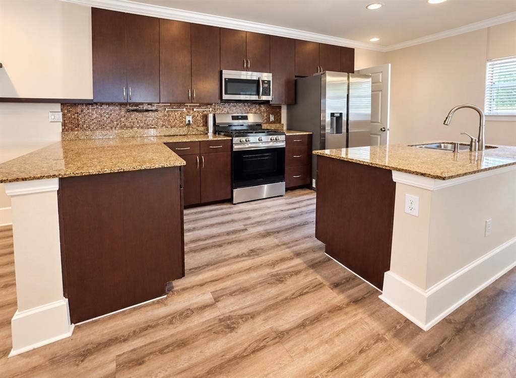 4227 Delano Place, Dallas, TX 75204 Kitchen featuring dark-finish cabinetry, stone-surface countertops, stainless steel appliances, a mosaic tile backsplash, and wood-finish flooring