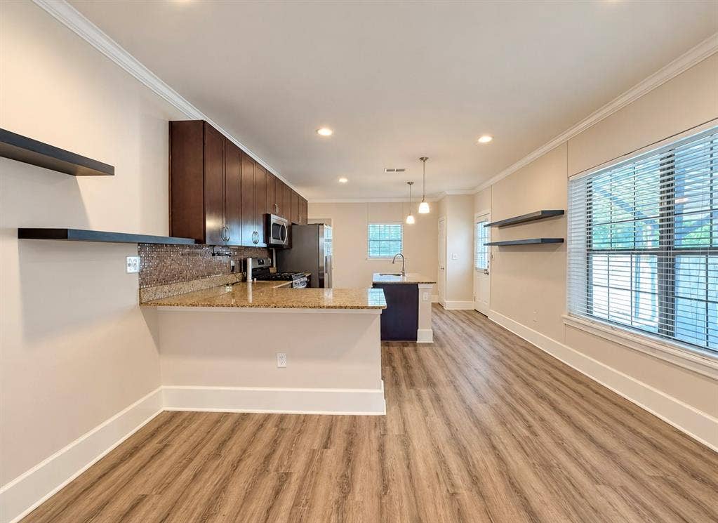 4227 Delano Place, Dallas, TX 75204 Kitchen featuring wood-finish flooring, dark wood cabinetry, stone countertops, mosaic tile backsplash, and floating wall shelves