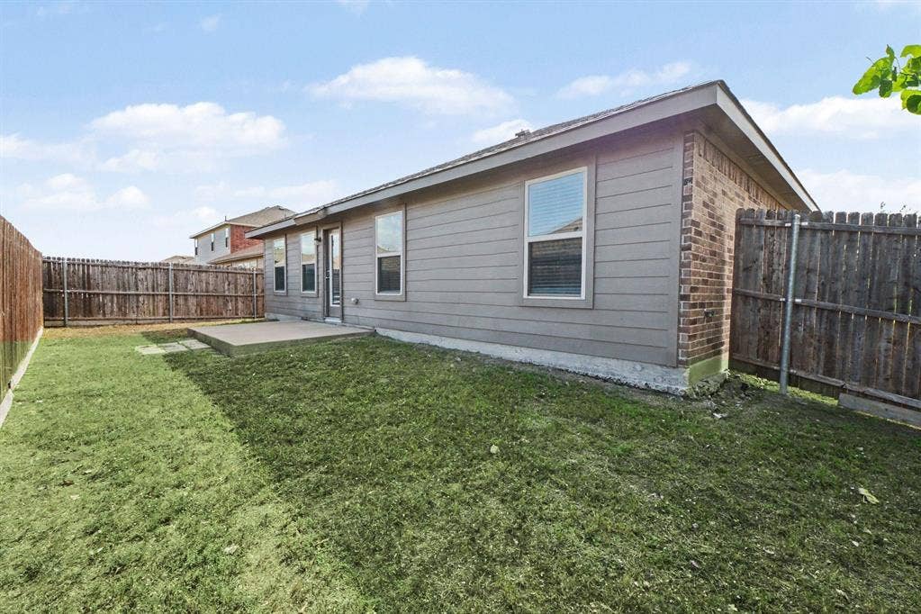 814 Rustic Meadows Trail, Princeton, TX 75407 Exterior rear elevation featuring horizontal siding, brick masonry, a concrete patio, and a wood privacy fence enclosing the lawn
