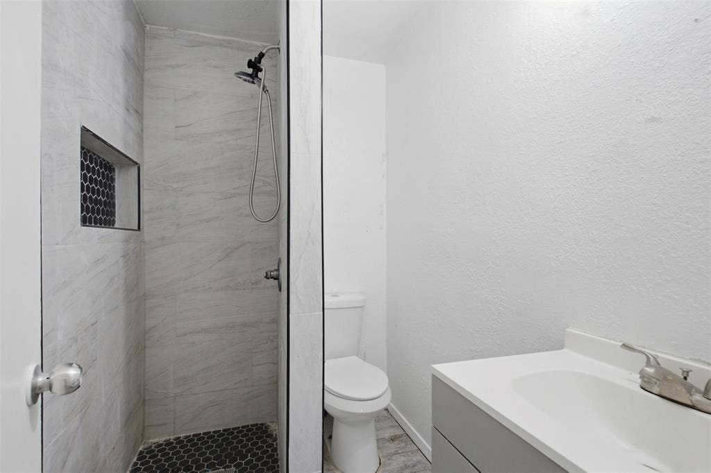 2009 S 1st Street, Garland, TX 75041 Bathroom featuring a walk-in shower with light-toned wall tile, a dark-toned hexagonal tile floor, and a built-in recessed niche
