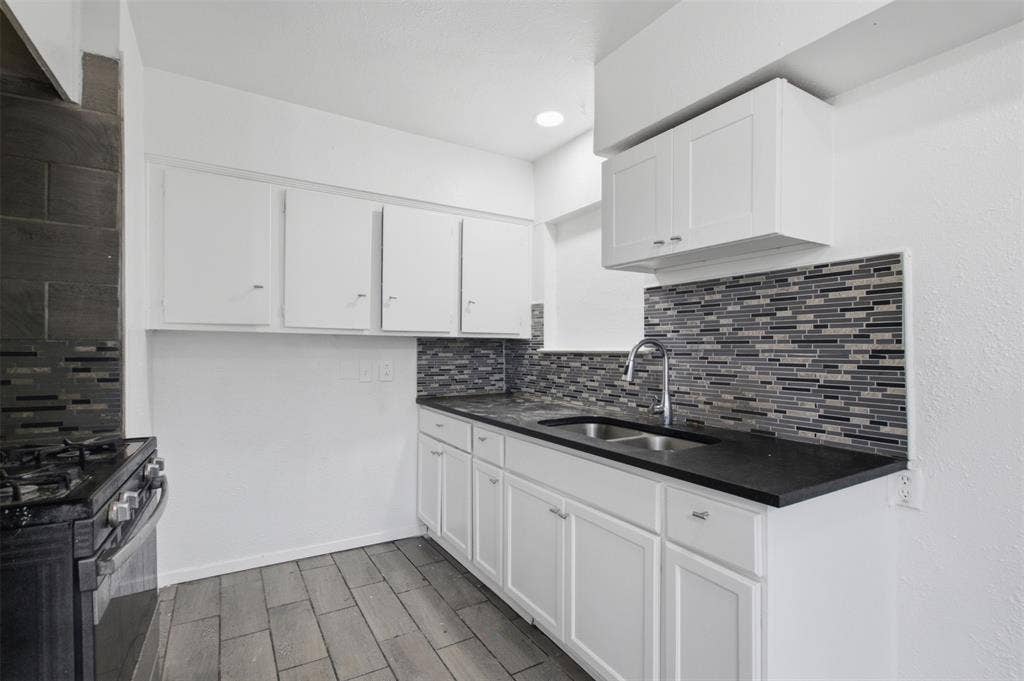 2009 S 1st Street, Garland, TX 75041 Kitchen featuring white cabinetry, dark countertops, a multi-tone linear tile backsplash, stainless steel double-basin sink with pull-down faucet, and wood-finish flooring
