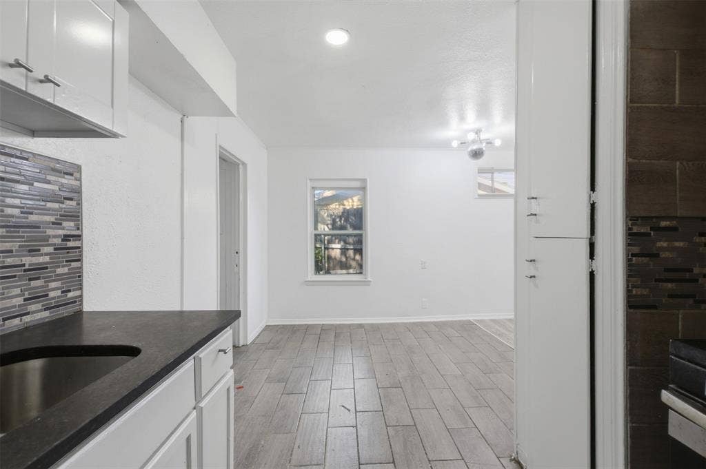 2009 S 1st Street, Garland, TX 75041 White cabinetry, dark countertops, wood-finish tile flooring, mosaic tile backsplash, and recessed ceiling lighting