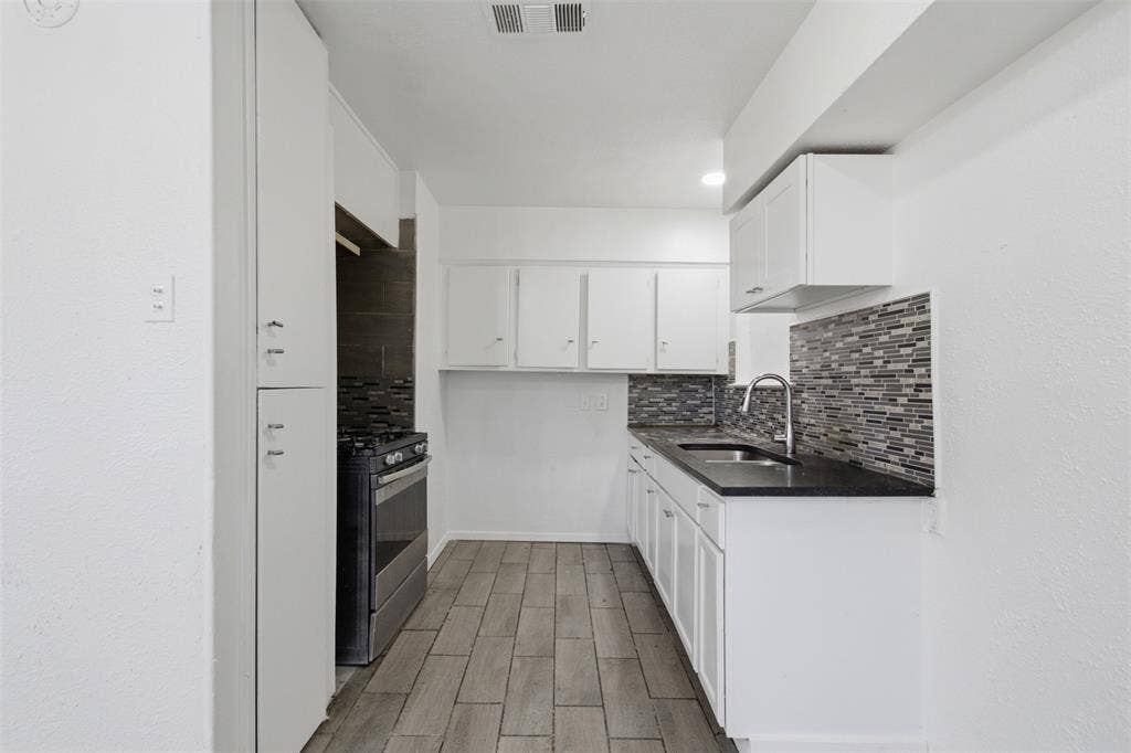 2009 S 1st Street, Garland, TX 75041 Kitchen featuring white cabinetry, wood-finish flooring, dark countertops, a stainless steel gas range, and a decorative tile backsplash