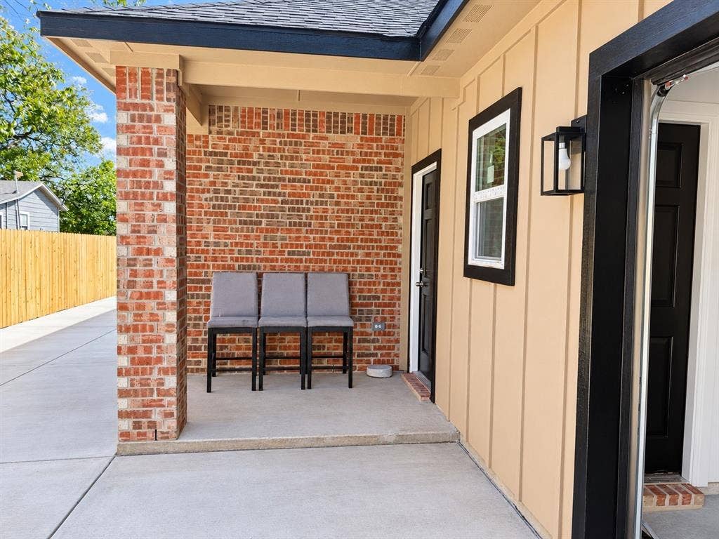 707 N Blanche Street, Terrell, TX 75160 Covered patio featuring a red brick accent wall, vertical wood-finish siding, concrete flooring, and a contemporary black exterior wall-mounted light fixture