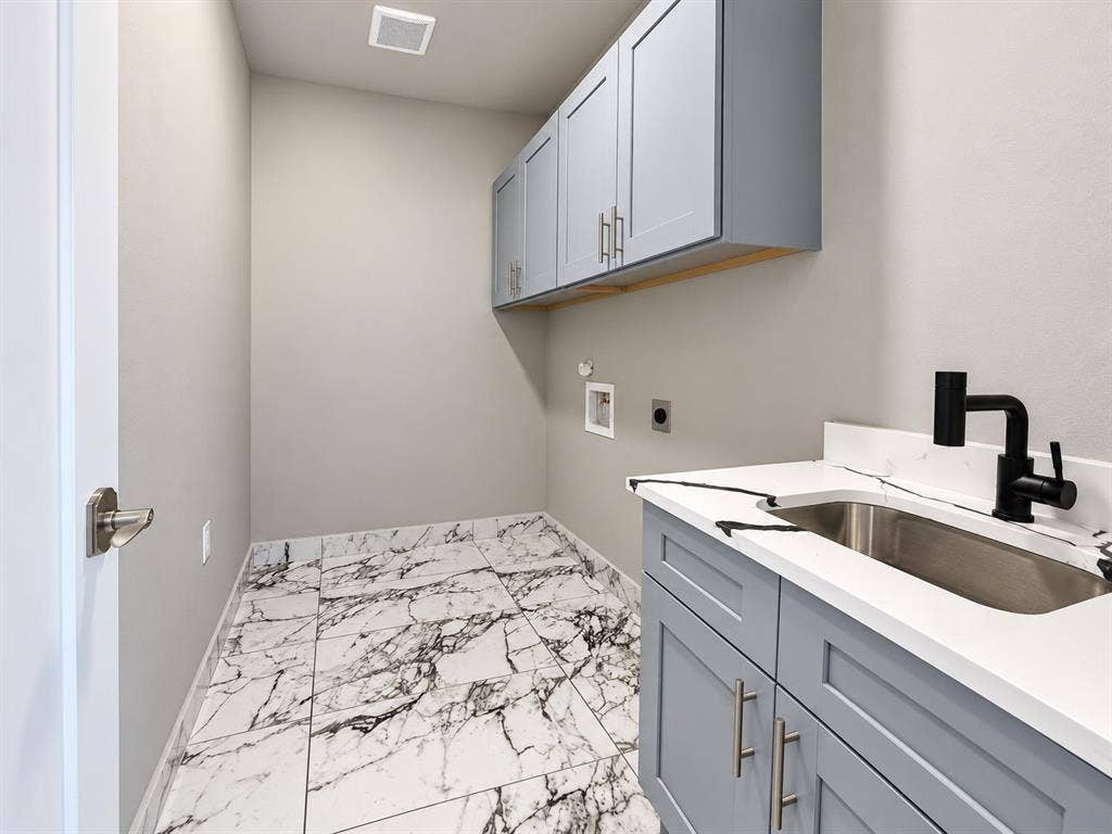 707 N Blanche Street, Terrell, TX 75160 Utility area featuring marble-patterned tile flooring, gray Shaker-style cabinetry, white solid-surface countertops with an integrated stainless steel sink, and matte black plumbing fixtures