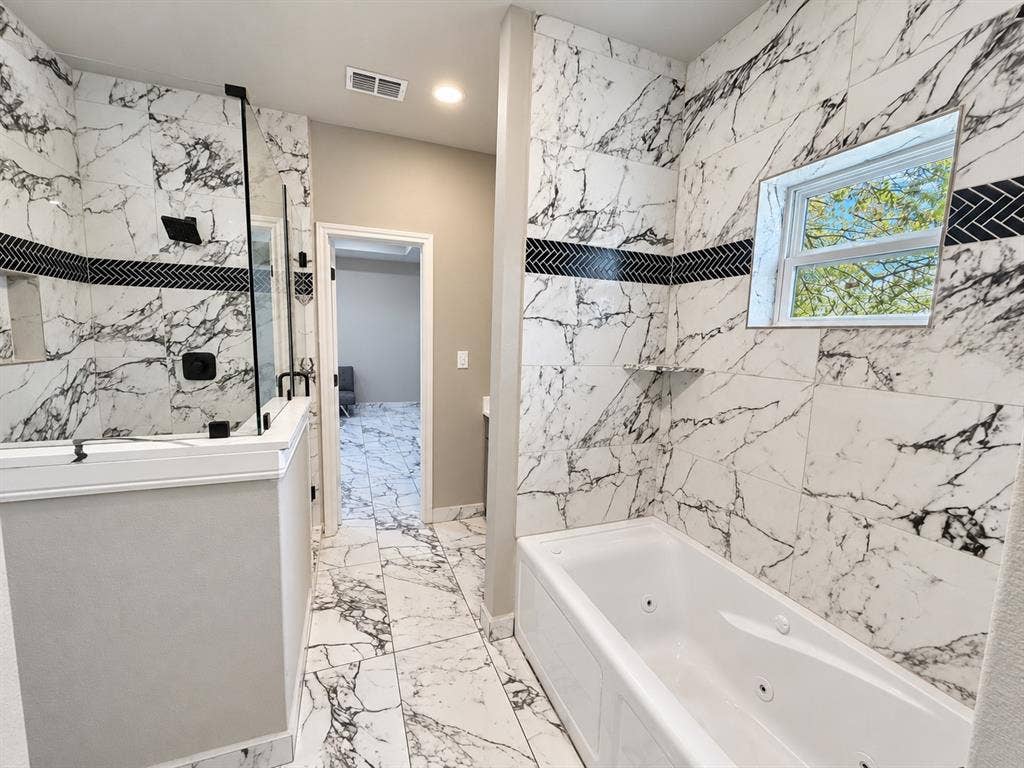 707 N Blanche Street, Terrell, TX 75160 Bathroom featuring large-format veined tile surround, a built-in jetted soaking tub, a walk-in glass-enclosed shower with matte black fixtures, and a decorative herringbone-patterned accent border
