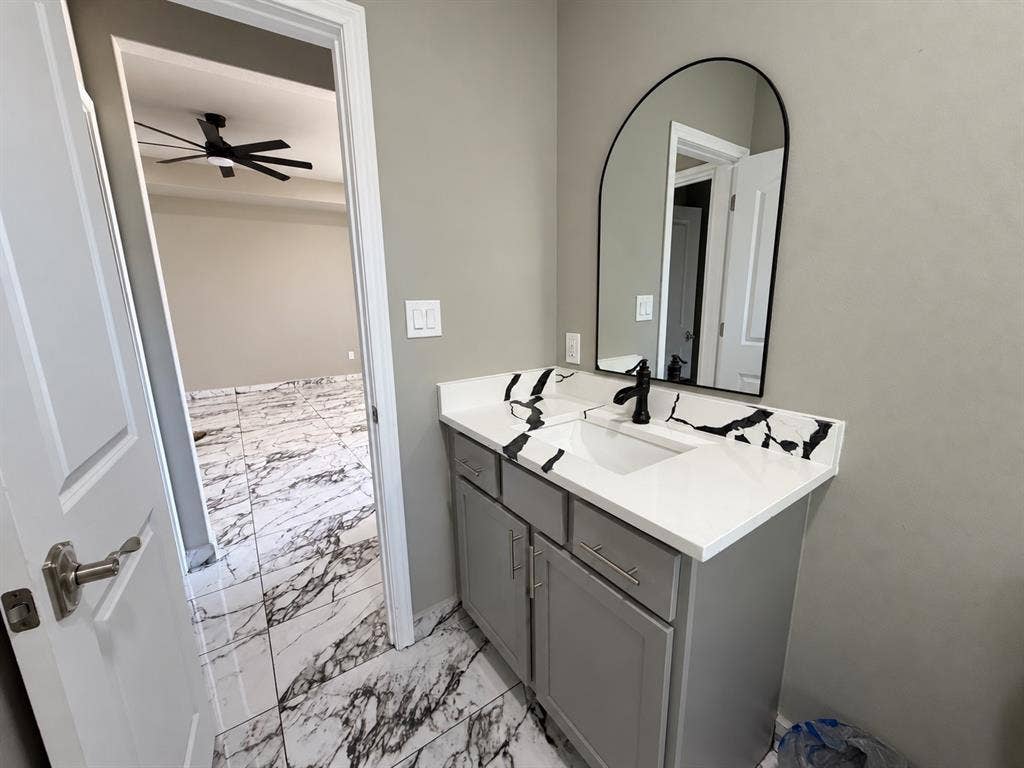 707 N Blanche Street, Terrell, TX 75160 Bathroom vanity featuring gray cabinetry, a white countertop with black veining, an integrated rectangular sink, a matte black faucet, and an arched wall-mounted mirror