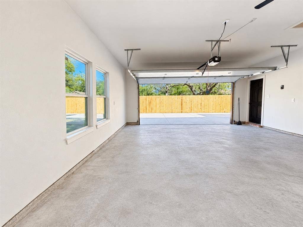 707 N Blanche Street, Terrell, TX 75160 Spacious multi-car garage featuring smooth-finished concrete flooring, dual-pane windows, a dark-finish entry door, and an automatic overhead door opener