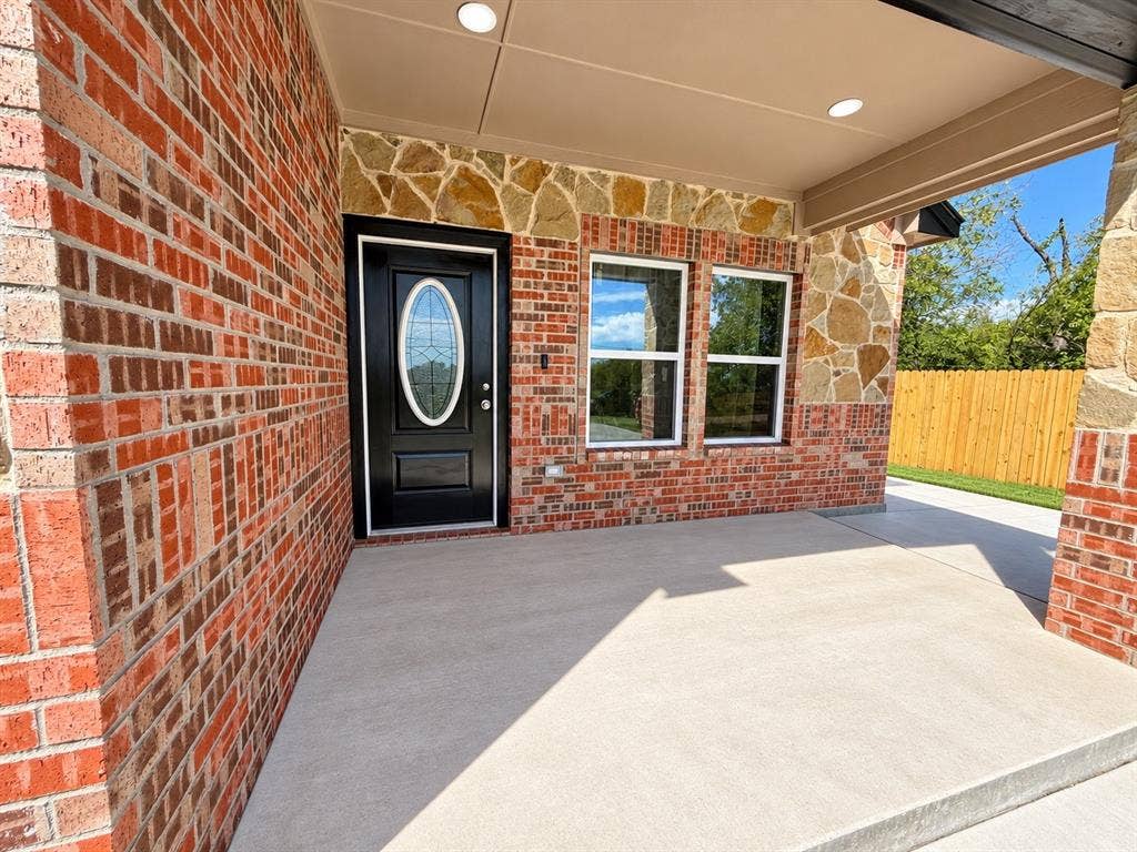 707 N Blanche Street, Terrell, TX 75160 Covered entryway featuring a brick and stone facade, concrete porch, and a front door with an oval glass insert