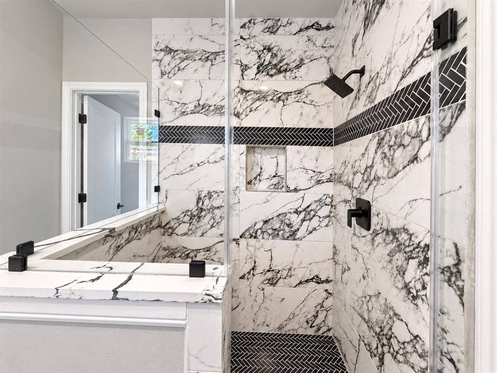 707 N Blanche Street, Terrell, TX 75160 Walk-in shower featuring floor-to-ceiling large-format veined tile, integrated wall niche, matte black fixtures, and a decorative herringbone tile accent border