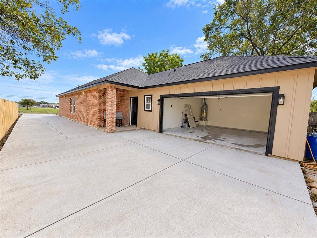707 N Blanche Street, Terrell, TX 75160 Exterior featuring a brick and board-and-batten siding facade, two-car garage with an open bay, extended concrete driveway, covered porch with a brick pillar, and shingle roofing