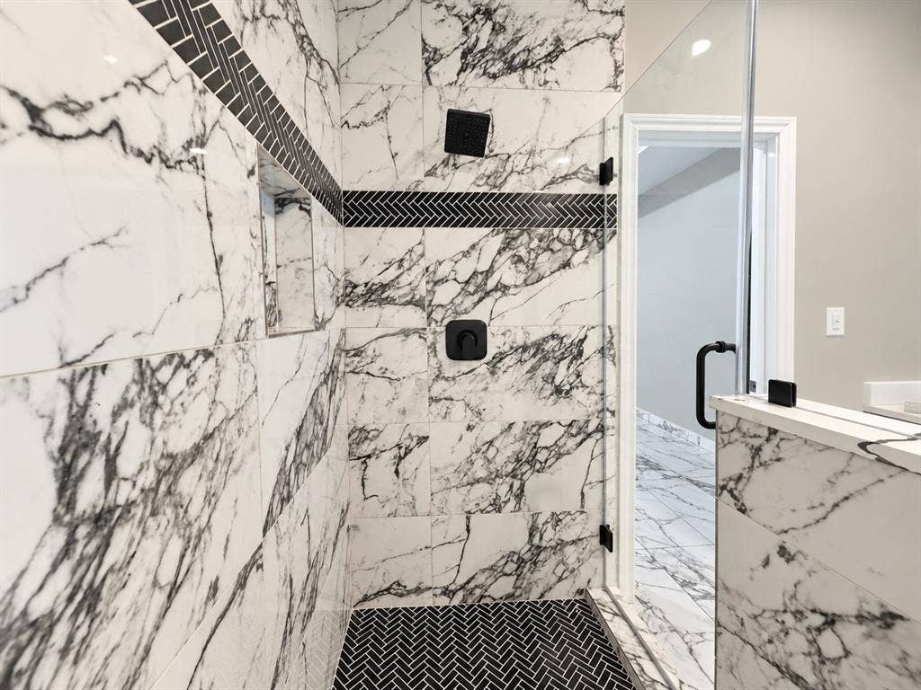 707 N Blanche Street, Terrell, TX 75160 Walk-in shower featuring large-format patterned wall tile, a herringbone tile floor, a built-in recessed niche, a rainfall showerhead, and a frameless glass enclosure